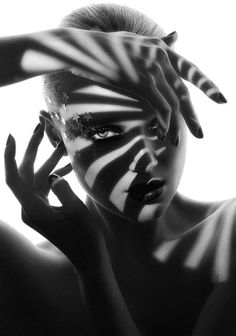 a woman with her hands on her head and face painted like zebra stripes, posing in front of a white background