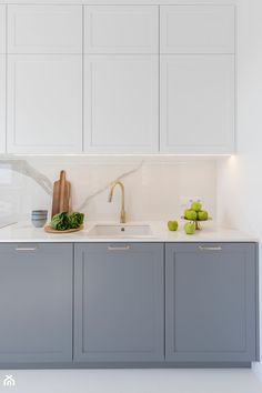 a kitchen with gray cabinets and white counter tops is seen in this image, there are green apples on the counter