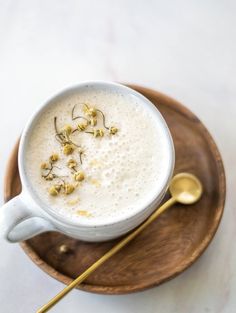 a cup of coffee with some flowers in it on a wooden plate next to a spoon