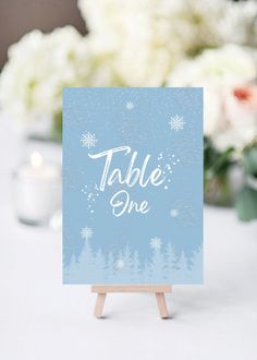 a table sign sitting on top of a wooden easel next to flowers and candles