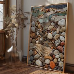 there is a painting made out of rocks and pebbles on the floor next to a vase with flowers in it