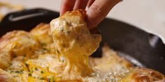 a person is dipping some food into a skillet with melted cheese and chives