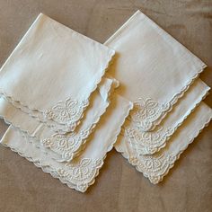 four white napkins with scalloped edges on a brown cloth covered tablecloth