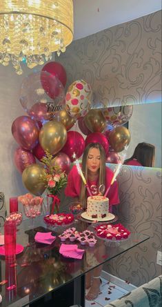 a woman sitting at a table with a cake and balloons