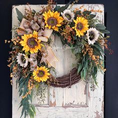 a wreath with sunflowers and greenery is hung on a door frame in front of an old wooden door