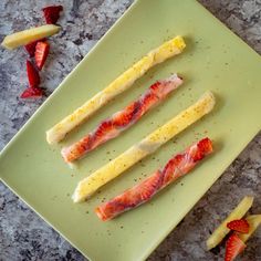 four pieces of food on a green plate next to sliced strawberries and lemon wedges