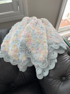 a crocheted blanket is sitting on top of a leather couch in front of a window