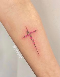 a small cross tattoo with pink flowers on the left side of the arm and behind it is an arrow