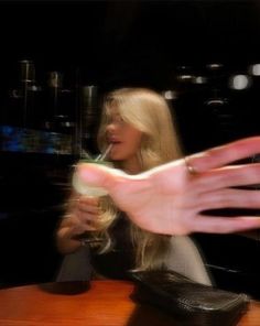 a woman sitting at a table with her hand reaching out to drink from a cup