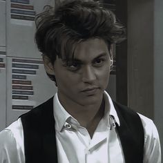 a young man wearing a vest and white shirt is looking at the camera while standing in front of lockers