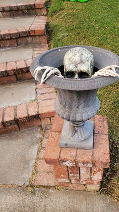 a cement bird bath sitting on top of a brick walkway next to grass and steps