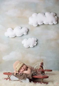 a baby sleeping on top of a wooden bench in front of clouds and a teddy bear