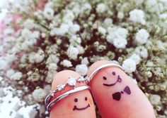 two fingers with smiley faces drawn on them, one has a ring and the other has a wedding band