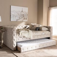 a white daybed sitting on top of a wooden floor next to a table with a lamp