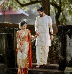 a man and woman holding hands while standing next to each other in front of trees