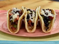 three tacos are sitting on a pink plate with white sauce and black olives