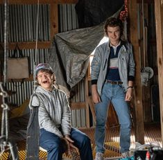 two young men sitting on top of a wooden bench in a room with metal pipes