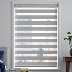 a living room with white walls and grey blinds on the window sill, in front of a gray couch