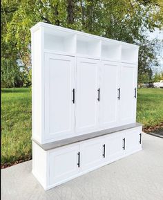 a large white cabinet sitting on top of a cement floor in front of trees and grass