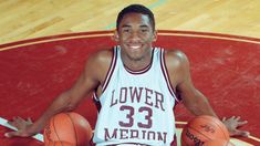 a man sitting on the floor with two basketballs in front of him and smiling