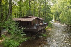 a cabin in the woods with a river running through it and trees lining the sides