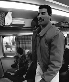 a man standing in the middle of a train with other people sitting on seats behind him