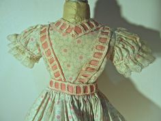 "We are pleased to offer for sale this charming, vintage floor length doll dress. The dress dates back to the 1950's and is a white cotton subdued print of circles with pink dots in the center. The fitted bodice has a modified \"V\" neck, short puff sleeves that are trimmed with white lace and a pink ribbon design of suspenders and waist band. The very full, floor length skirt has two rows of pink piping that has an added white lace ruffled trim at the hem. The inside of the skirt has an attache Vintage Floor, Floor Length Skirt, Ribbon Design, Front Bottoms, Lace Ruffle, Doll Clothing, Vintage Cotton, Pink Ribbon, Fitted Bodice