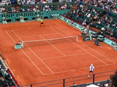 two people playing tennis on a clay court in front of an audience at a tennis match