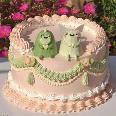 a pink cake with two green birds sitting on it's sides and flowers in the background