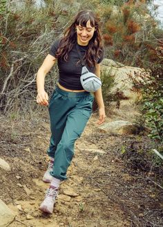 a woman walking down a dirt path carrying a frisbee in her right hand