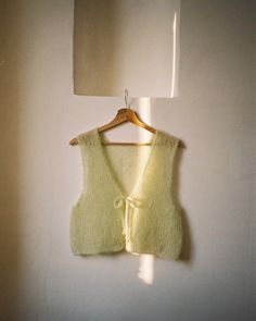 a light green sweater vest hanging on a white wall next to a lamp and mirror