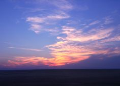 the sun is setting over an ocean with some clouds