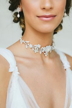 a woman in a white dress wearing a necklace and earrings with flowers on the neck