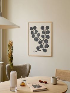 a table with two cups and a vase on it in front of a framed art piece