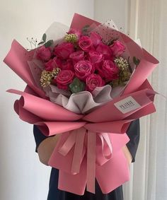 a woman holding a bouquet of pink roses in her hands, wrapped in paper and tied with ribbon