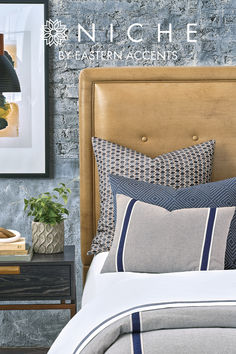 a bed with blue and white pillows on it next to a brick wall in a bedroom