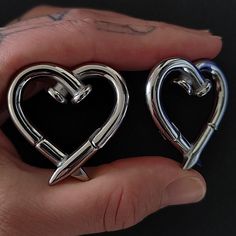 two silver heart shaped earrings in the palm of someone's hand