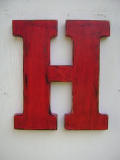 the letter h is made out of wood and sits on a white wall with red paint