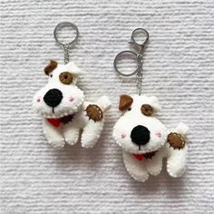 two stuffed dogs are hanging from key chains on a white surface, one is wearing a red collar and the other has a brown nose