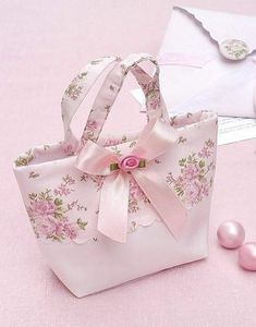 a pink flowered bag sitting on top of a table next to pearls and an envelope