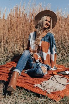 a woman sitting on top of a blanket holding a glass of wine