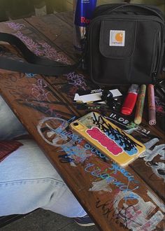 a table topped with lots of graffiti and other items next to a black bag on top of it