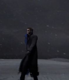 a man walking in the snow with his coat over his head and sunglasses on,