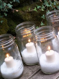 four mason jars filled with white sand and lit candles