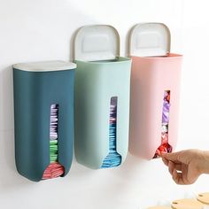 three colorful toothbrushes are hanging on the wall next to a person's hand