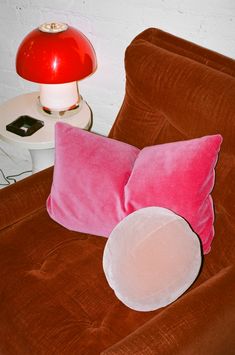 a pink pillow sitting on top of a brown chair next to a red table lamp