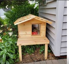 a small wooden bird house sitting on top of a table next to a flower garden