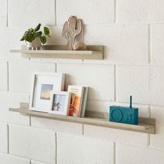 two shelves with books and pictures on them against a white brick wall in a room