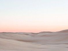 two people are walking in the sand dunes at sunset or dawn with their skis on