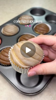 someone is holding a cupcake in front of a muffin tin with chocolate frosting